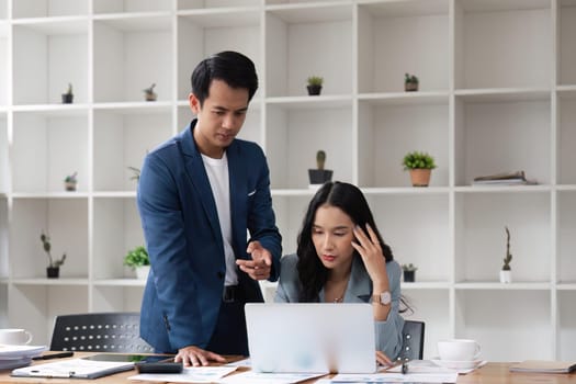 Two business people being stressed while working on a laptop in an office, Business partners working together, Collaborating teamwork analyzing paperwork data, business reports.