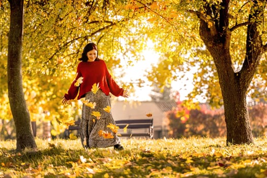 Pretty girl posing in autumn park with yellow leaves. Attractive young woman wearing cozy beautiful dress in fall season with golden foliage at nature