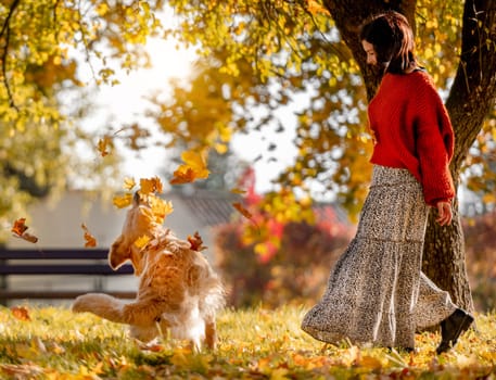 Beautiful girl with golden retriever dog holding yellow leaf in hand in autumn park. Pretty young woman playing with purebred doggy labrador at fall season at nature