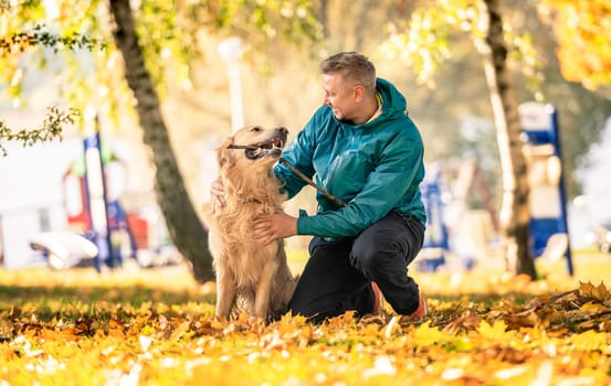 Man playing with his dog golden retriever in autumn park