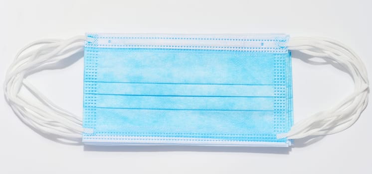 Disposable blue medical face mask against virus protection on a white background, top view