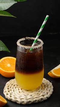 Iced coffee with orange juice in a transparent glass, refreshing bumble coffee on the table, black background