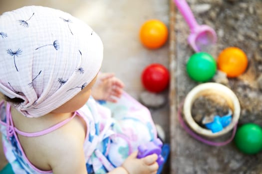 toddler girl playing in sand in sandbox with various toys on outdoor playground