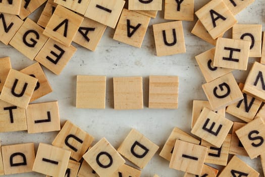 Top down view, pile of square wooden blocks with letters on white board. Three empty tiles for your text.