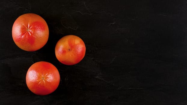 Top down view, three pink grapefruits on black marble board, banner with space for text at right side.