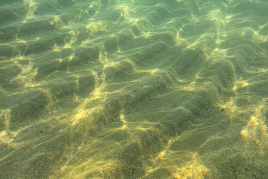 Underwater photo - sun shines on sand "dunes" on sea floor in shallow water near beach, abstract marine background.