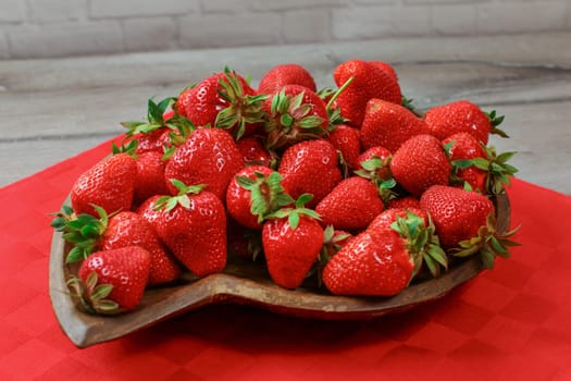 Closeup, strawberries on wooden carved bowl, red tablecloth under.