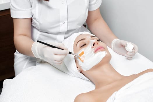 beautician applies the mask to the face of beautiful young woman in the spa salon. spa treatments