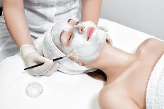 beautician applies the mask to the face of beautiful young woman in the spa salon. spa treatments closeup