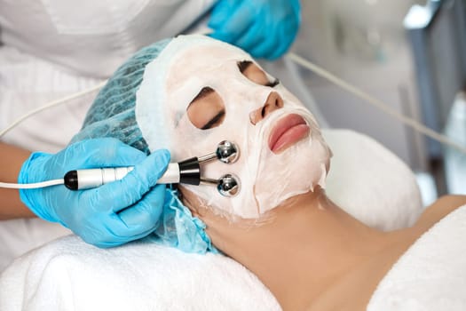 beautician applies face textile mask on beautiful young woman in Spa salon. cosmetic procedure skin care