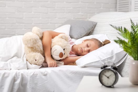 Cute little child girl sleeping with teddy bear in her bed