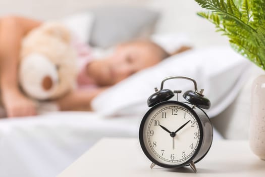 Cute little child girl sleeping with teddy bear in her bed. focus on clock