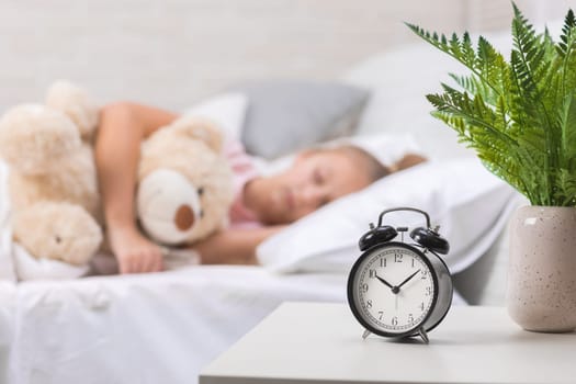 Cute little child girl sleeping with teddy bear in her bed. focus on clock