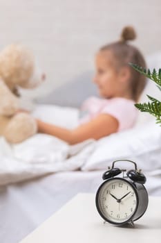 adorable little child girl playing with teddy bear in bed in morning. focus on clock