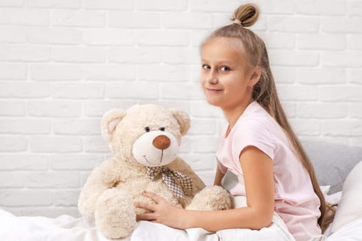 adorable little child girl playing with teddy bear in bed in morning