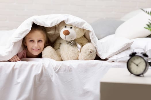 adorable little child girl playing with teddy bear in bed in morning