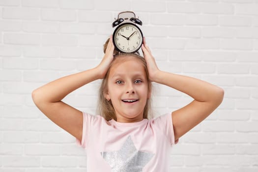 cute surprised little child girl in pyjamas with clock in bed. good morning