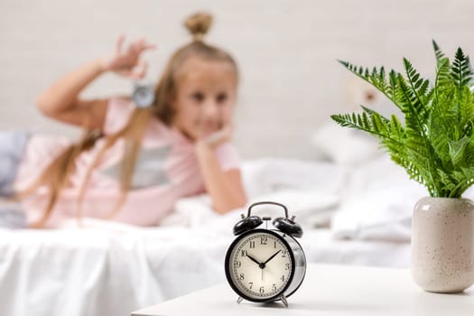 cute little child girl in pyjamas with clock in bed. good morning. focus on clock