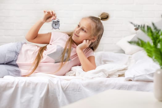 cute little child girl in pyjamas with clock in bed. good morning