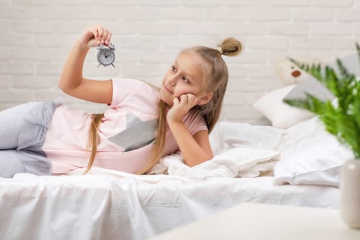 cute little child girl in pyjamas with clock in bed. good morning
