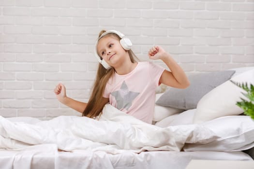 little child baby girl listening to the music with the headphones and dancing on bed. happy morning