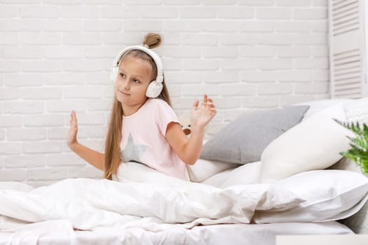little child baby girl listening to the music with the headphones and dancing on bed. happy morning