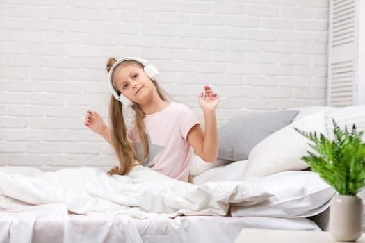 happy little child baby girl listening to the music with the headphones and dancing on bed. happy morning
