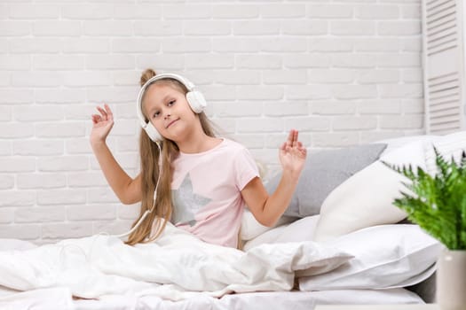 happy little child baby girl listening to the music with the headphones and dancing on bed. happy morning