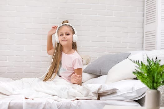 happy little child baby girl listening to the music with the headphones and dancing on bed. happy morning