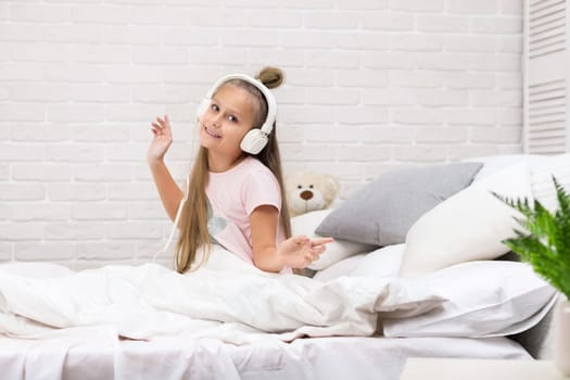 little child baby girl listening to the music with the headphones and dancing on bed. happy morning