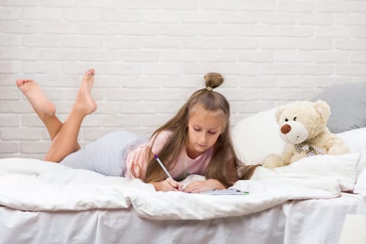 cute little girl drawing pictures while lying on bed. Kid painting at home