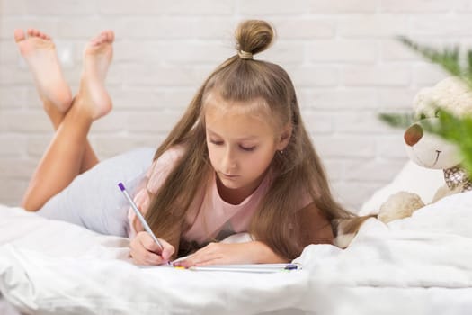 cute little girl drawing pictures while lying on bed. Kid painting at home. happy morning