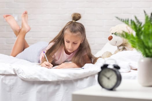 cute little girl drawing pictures while lying on bed. Kid painting at home