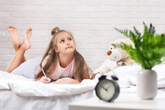 cute little girl drawing pictures while lying on bed. Kid painting at home. happy morning