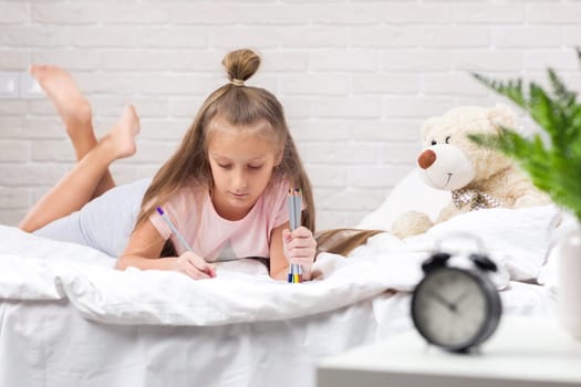 cute little girl drawing pictures while lying on bed. Kid painting at home