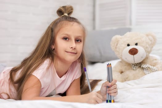 cute little girl drawing pictures while lying on bed. Kid painting at home. happy morning