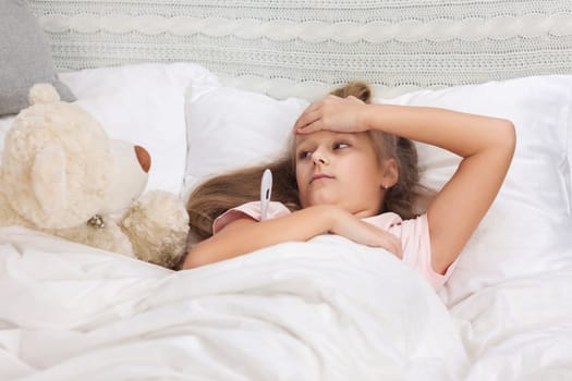Sick little child girl lying in bed with thermometer. Cold flu season