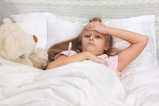 Sick little child girl lying in bed with thermometer. Cold flu season