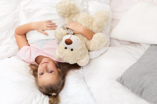 adorable little child girl lying with teddy bear in bed in morning. top view