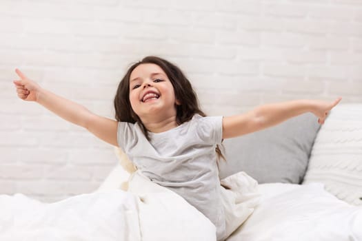 cute happy smiling little child girl wakes up from sleep in bed in the morning