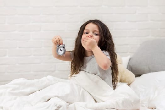 cute little child girl in pyjamas with clock in bed. good morning