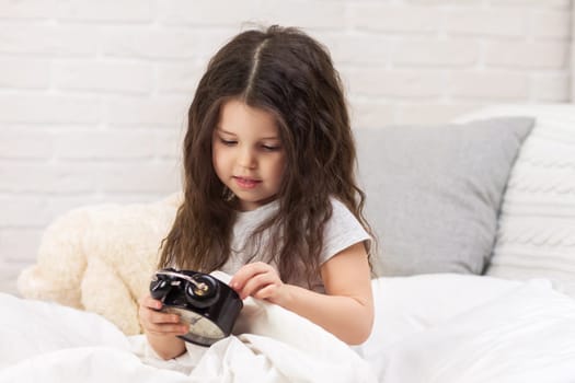 cute little child girl in pyjamas with clock in bed. good morning
