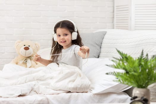 little child baby girl listening to the music with the headphones on bed. happy morning