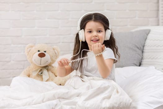 little child baby girl listening to the music with the headphones on bed. happy morning
