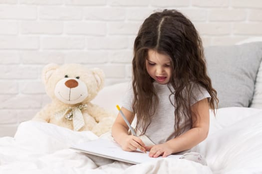 cute little girl drawing pictures while lying on bed. Kid painting at home