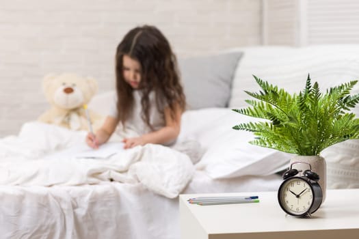 cute little girl drawing pictures while lying on bed. Kid painting at home