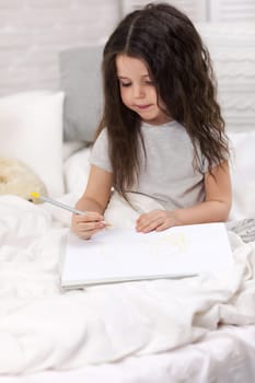 cute little girl drawing pictures while lying on bed. Kid painting at home