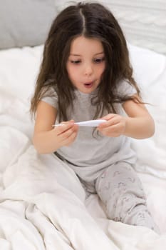 Sick surprised little child girl looking at thermometer. Cold flu season
