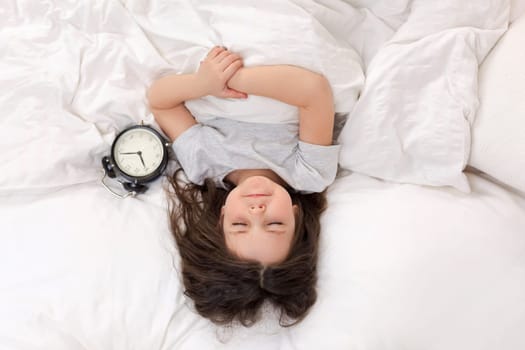 cute little child girl in pyjamas with clock in bed. good morning. top view