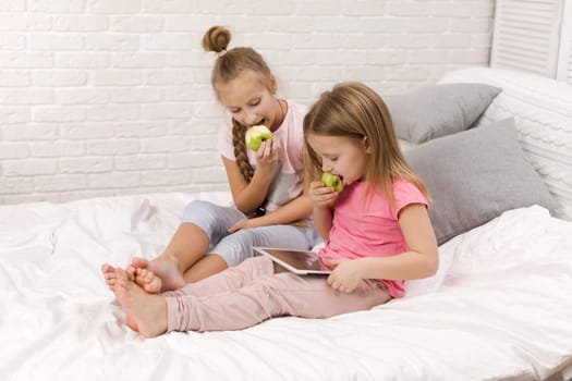 two cute children girls use digital tablet in bed. child playing on tablet pc.